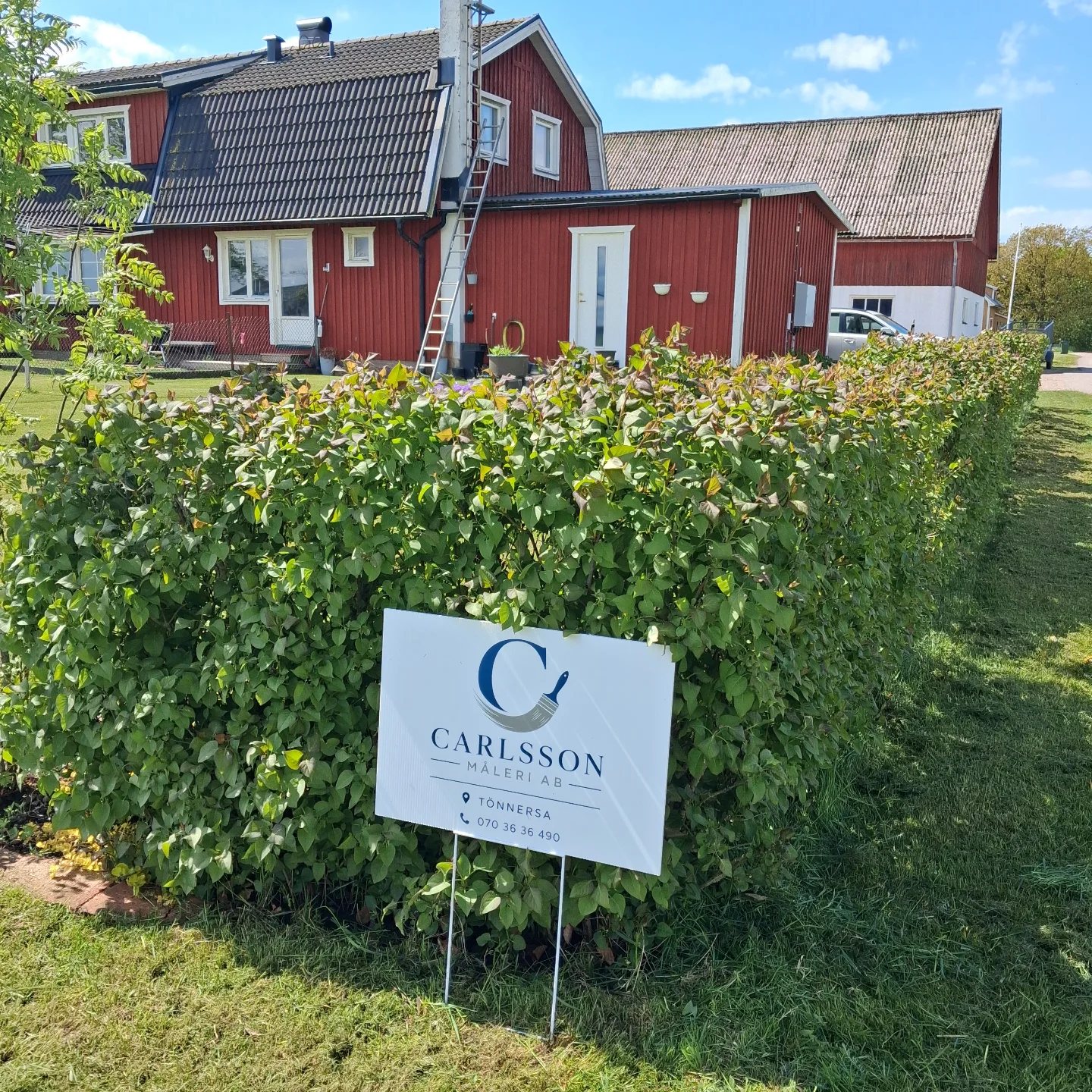 Rött trähus med Carlsson Måleris skylt framför häcken